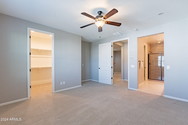 unfurnished bedroom featuring a closet, ceiling fan, light carpet, and a walk in closet