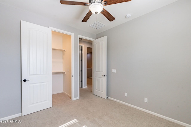 unfurnished bedroom featuring light carpet, a walk in closet, a closet, and ceiling fan