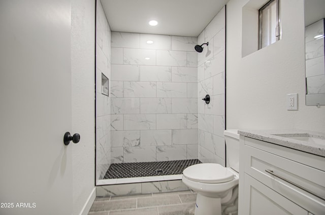 bathroom with tiled shower, toilet, recessed lighting, marble finish floor, and vanity