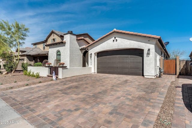 mediterranean / spanish-style home featuring a gate, fence, stucco siding, a garage, and decorative driveway