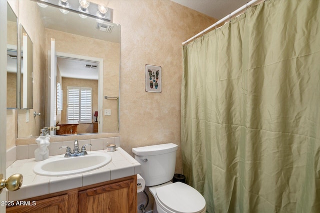 full bath with visible vents, toilet, vanity, and a textured wall