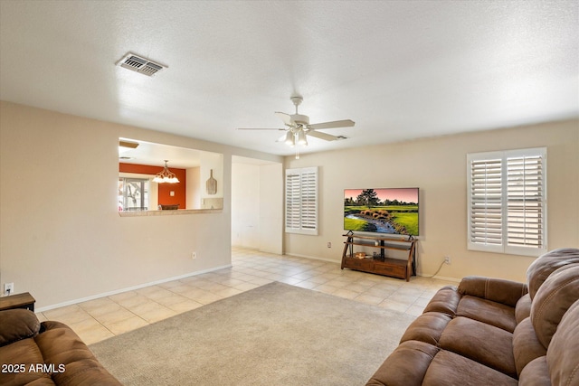 carpeted living room featuring tile patterned floors, visible vents, ceiling fan with notable chandelier, and baseboards