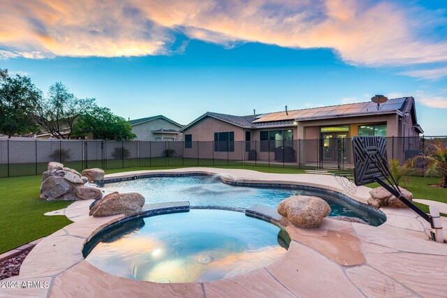 pool at dusk with a patio, a yard, an in ground hot tub, and pool water feature