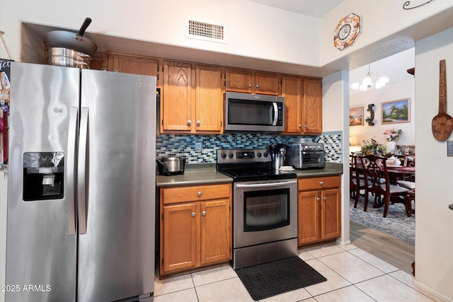 kitchen with appliances with stainless steel finishes, an inviting chandelier, hanging light fixtures, light tile patterned flooring, and decorative backsplash