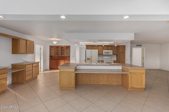 kitchen with a spacious island, sink, light tile patterned flooring, and white appliances