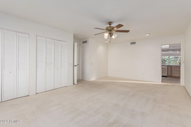 unfurnished bedroom featuring light carpet, ensuite bathroom, two closets, and ceiling fan