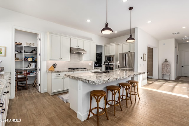 kitchen with stainless steel appliances, white cabinetry, and a kitchen island with sink