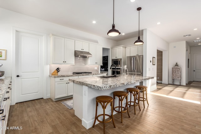 kitchen featuring a center island with sink, white cabinets, decorative light fixtures, light hardwood / wood-style floors, and stainless steel appliances