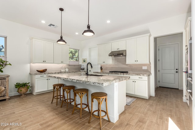 kitchen with light wood-type flooring, sink, decorative light fixtures, a center island with sink, and white cabinets