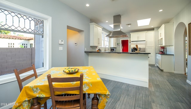 kitchen featuring kitchen peninsula, backsplash, white cabinetry, island range hood, and stainless steel refrigerator