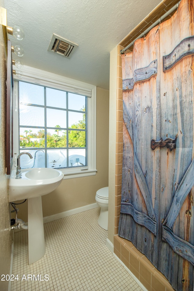 bathroom featuring toilet, tile patterned floors, a textured ceiling, and a shower with curtain