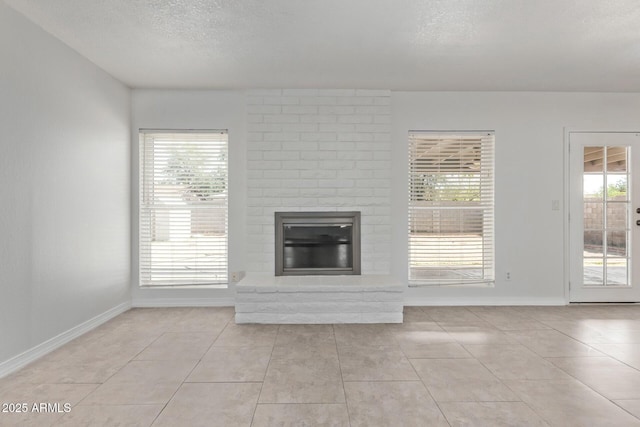 unfurnished living room featuring baseboards, a textured ceiling, light tile patterned flooring, and a brick fireplace