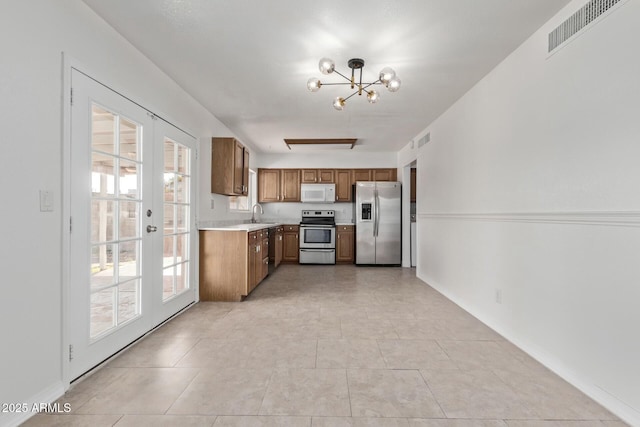 kitchen featuring an inviting chandelier, brown cabinetry, appliances with stainless steel finishes, light countertops, and visible vents