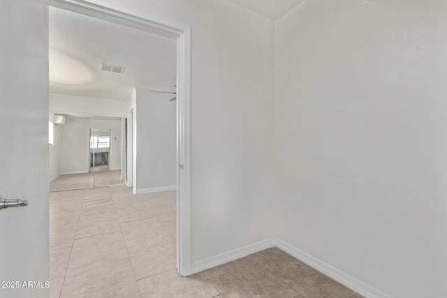 hall with baseboards, visible vents, and light tile patterned floors