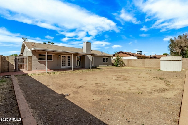 back of property featuring a chimney, a gate, a storage shed, french doors, and a fenced backyard