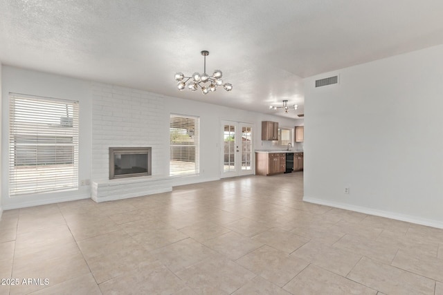 unfurnished living room with a chandelier, light tile patterned floors, baseboards, visible vents, and a textured ceiling