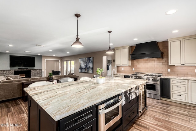 kitchen with high end range, a center island with sink, light stone countertops, custom range hood, and cream cabinetry