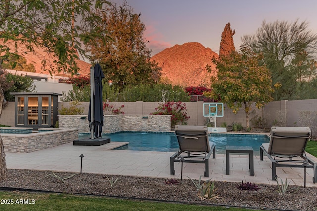 pool at dusk with a patio area, a mountain view, a hot tub, and a grill