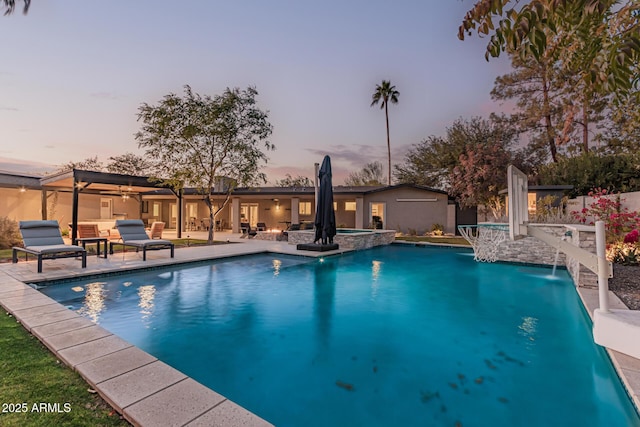 pool at dusk featuring pool water feature, a patio, and an in ground hot tub