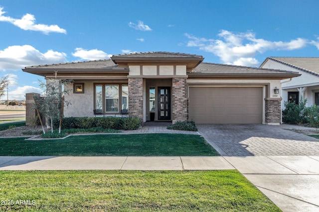 prairie-style house with an attached garage, a front yard, decorative driveway, and stucco siding