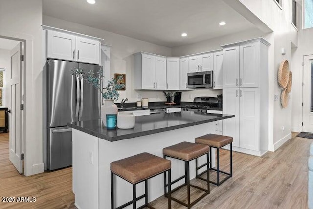 kitchen with a kitchen island, appliances with stainless steel finishes, a breakfast bar, white cabinets, and light hardwood / wood-style flooring