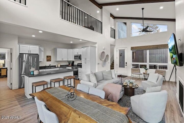 living room with sink, a high ceiling, ceiling fan, light hardwood / wood-style floors, and beam ceiling