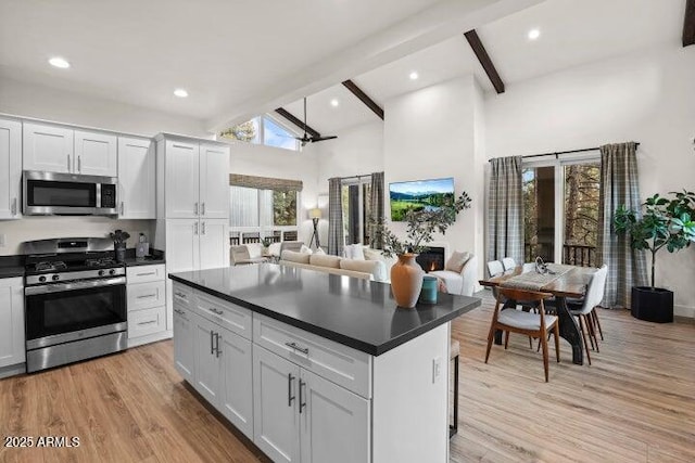 kitchen featuring beamed ceiling, appliances with stainless steel finishes, light hardwood / wood-style flooring, and white cabinets