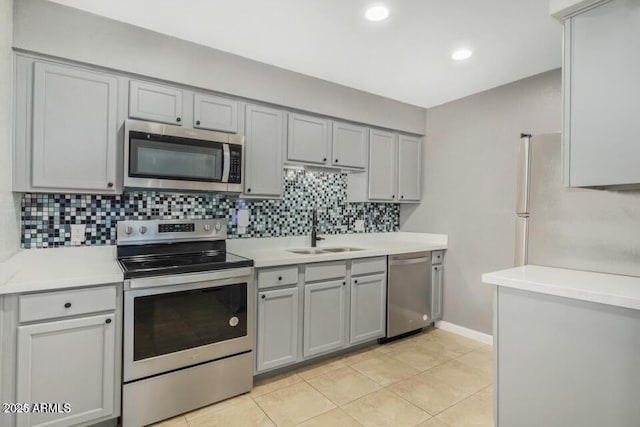 kitchen with gray cabinetry, a sink, stainless steel appliances, light countertops, and decorative backsplash