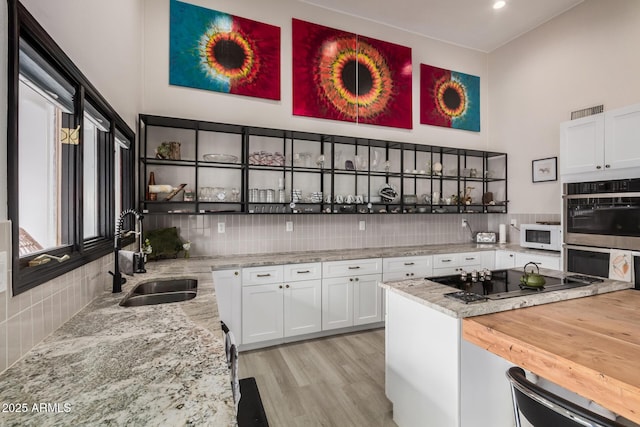 kitchen with backsplash, stainless steel double oven, white cabinets, a sink, and black electric cooktop