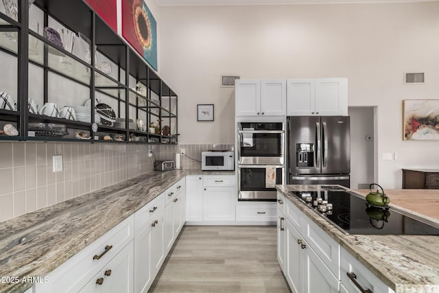 kitchen with appliances with stainless steel finishes, white cabinets, visible vents, and backsplash