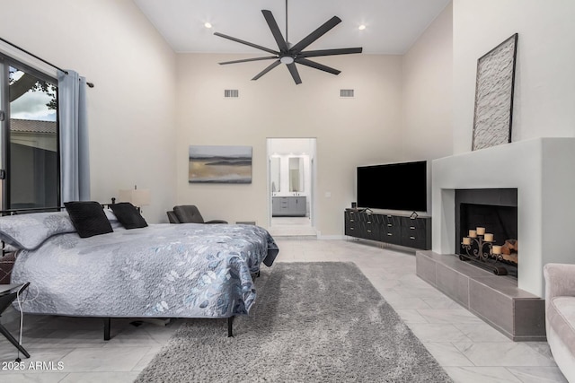 bedroom with a towering ceiling, a tile fireplace, visible vents, and connected bathroom