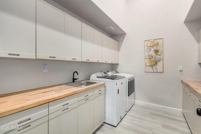 washroom featuring washing machine and dryer, a sink, baseboards, cabinet space, and light wood finished floors