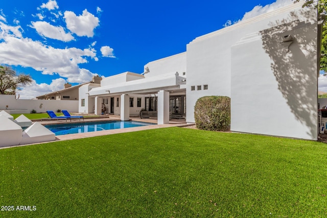 rear view of property with a patio, fence, a lawn, a fenced in pool, and stucco siding