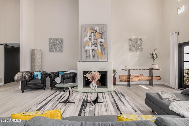 living area featuring a fireplace with raised hearth, wood finished floors, a towering ceiling, and baseboards