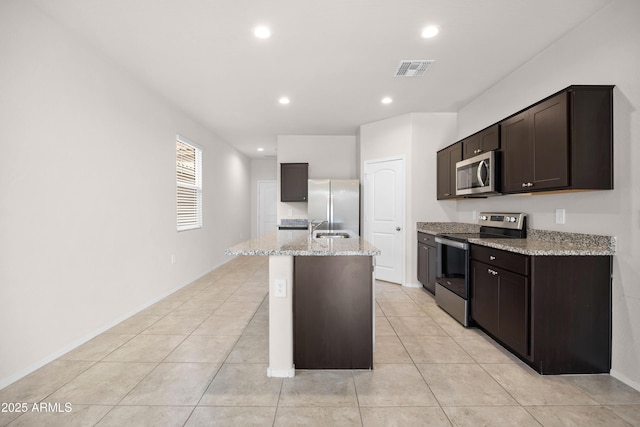 kitchen featuring a center island with sink, visible vents, light stone countertops, stainless steel appliances, and a sink