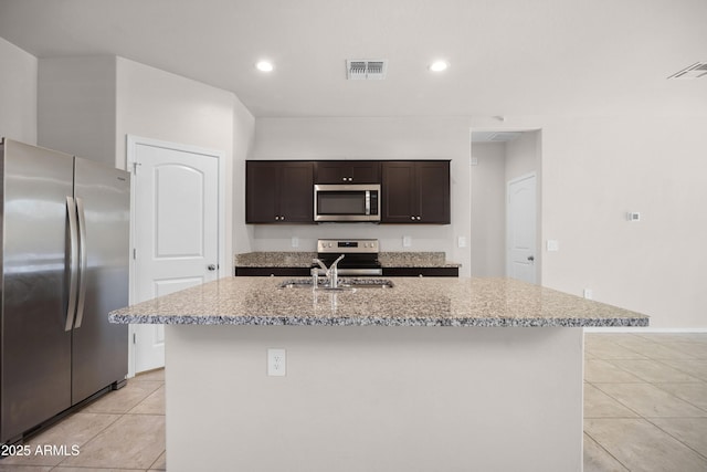 kitchen with stainless steel appliances, an island with sink, visible vents, and dark brown cabinetry