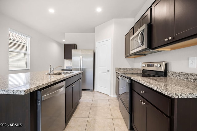 kitchen with light tile patterned floors, an island with sink, stainless steel appliances, dark brown cabinets, and a sink