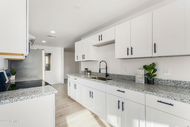 kitchen featuring black range, sink, light hardwood / wood-style flooring, light stone counters, and white cabinetry