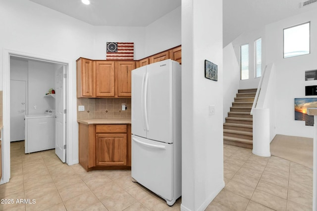 kitchen featuring light tile patterned floors, washer / clothes dryer, light countertops, backsplash, and freestanding refrigerator