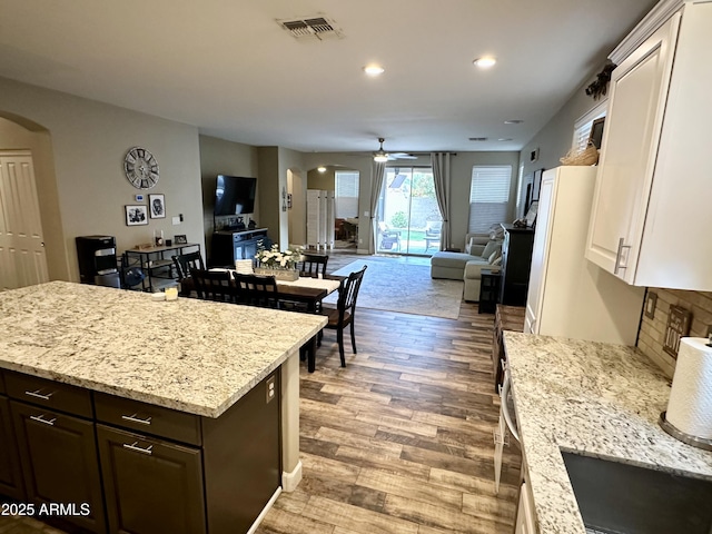 kitchen with visible vents, arched walkways, open floor plan, a ceiling fan, and light wood-style flooring