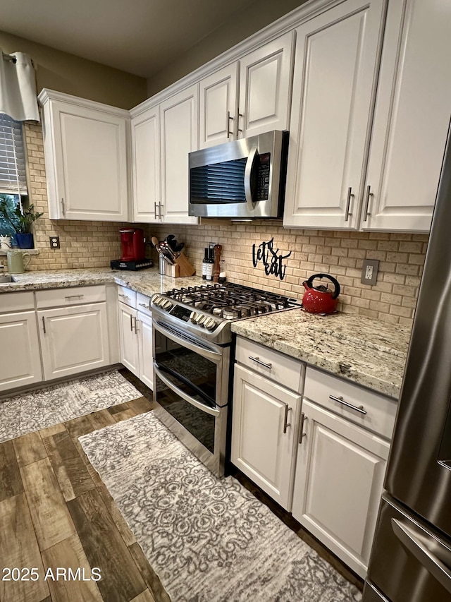 kitchen with tasteful backsplash, white cabinets, wood finished floors, light stone counters, and stainless steel appliances