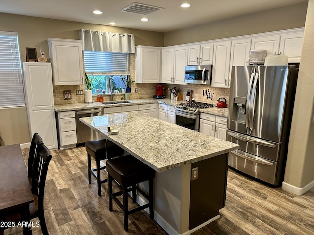 kitchen with visible vents, white cabinets, a sink, wood finished floors, and stainless steel appliances