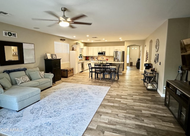 living room with visible vents, baseboards, arched walkways, ceiling fan, and light wood finished floors