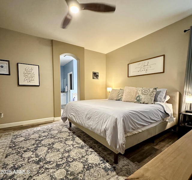 bedroom featuring ceiling fan, connected bathroom, arched walkways, wood finished floors, and baseboards
