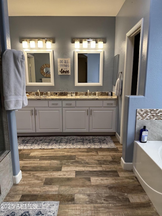 full bath with a sink, a bath, double vanity, and wood finished floors
