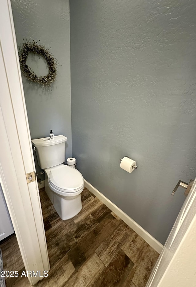 bathroom with a textured wall, baseboards, toilet, and wood finished floors
