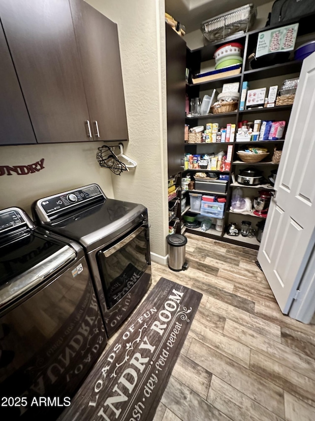 clothes washing area with separate washer and dryer, wood finished floors, a textured wall, and cabinet space