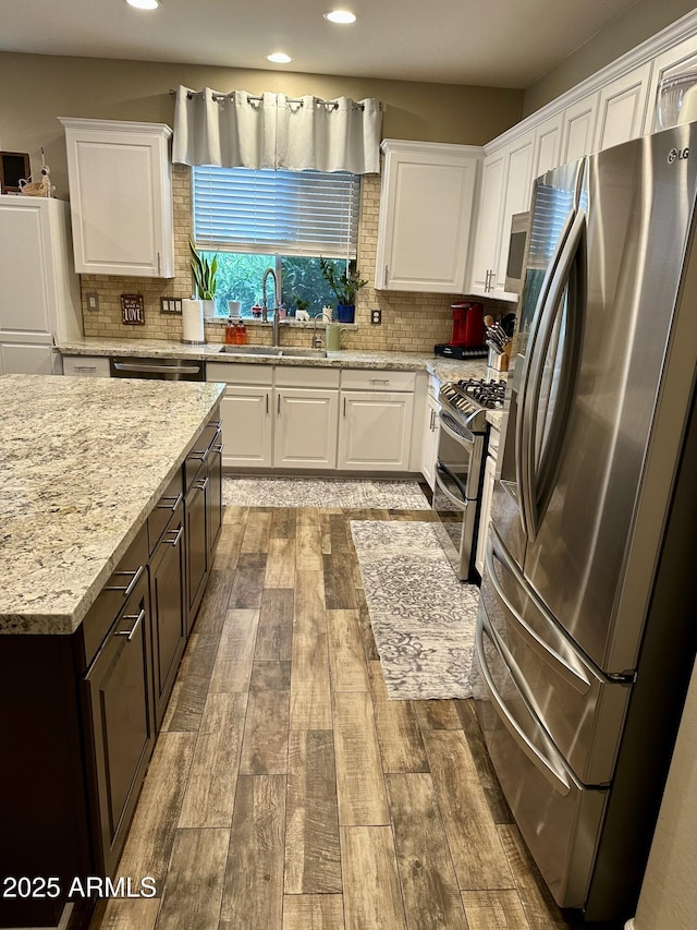 kitchen with white cabinets, a sink, wood tiled floor, stainless steel appliances, and backsplash
