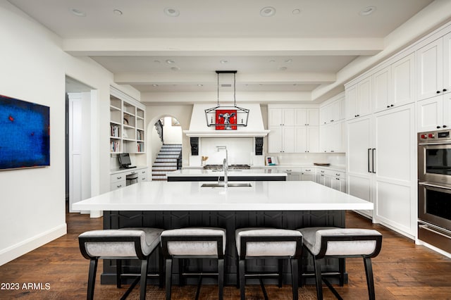 kitchen featuring a center island with sink, beam ceiling, dark wood-type flooring, and decorative light fixtures