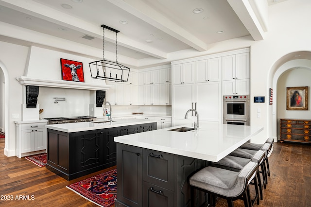 kitchen featuring sink, a center island with sink, dark wood-type flooring, and beam ceiling